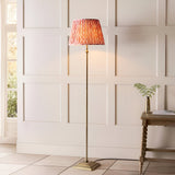 Endon Caldmere Ikat floor lamp with antique brass stand and pleated coral pink Ikat shade, placed by a panelled wall beside a wooden console table.