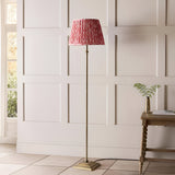 Endon Caldmere floor lamp with antique brass stem and stepped base, topped with a pleated coral pink Ikat fabric shade, in a panelled hallway.