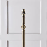 Close-up of the Endon Caldmere floor lamp's antique brass stem with B22 lamp holder and turned ball detail, against a white panelled door.