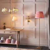 Endon Caldmere floor lamp with antique brass stand and coral pink Ikat pleated shade in a panelled room with matching table lamp, wall light and chandelier.
