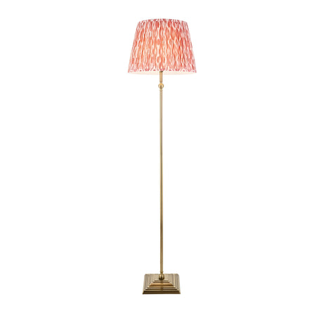Endon Caldmere floor lamp with antique brass stem and stepped square base, topped with a pleated coral pink Ikat fabric shade, on a white background.