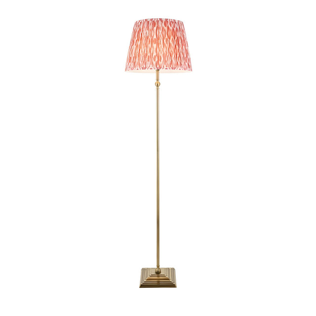 Endon Caldmere floor lamp with antique brass stem and stepped square base, topped with a pleated coral pink Ikat fabric shade, on a white background.