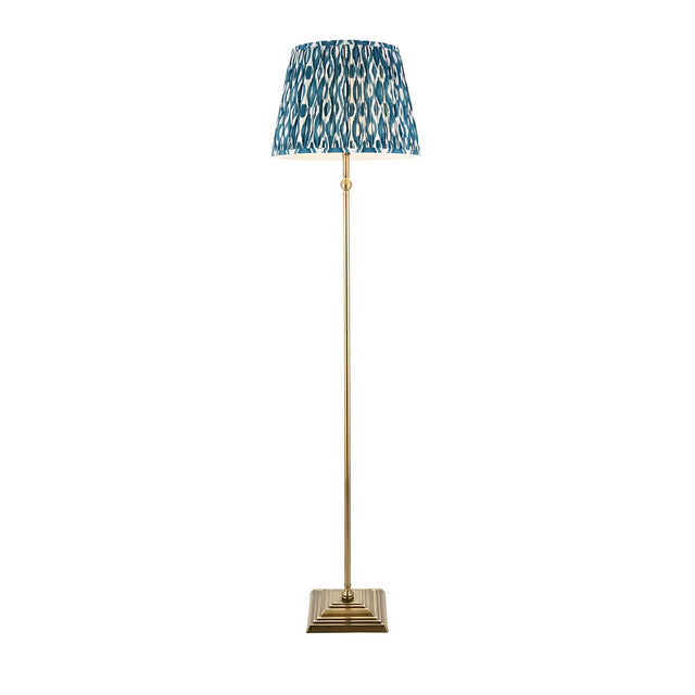 Endon Caldmere floor lamp with antique brass stem and stepped square base, topped with a pleated marlin blue Ikat fabric shade on a white background.