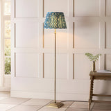 Endon Caldmere floor lamp with antique brass stem and stepped base, topped with a pleated marlin blue Ikat shade, beside a panelled wall.