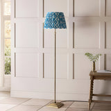 Endon Caldmere floor lamp with antique brass stem and stepped base, topped by a pleated marlin blue Ikat shade, in a panelled hallway setting.