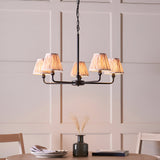 Caldmere 5 Light Ikat Pendant in Natural, with pleated fabric taper shades on a matt black metal frame, hung above a dining table.