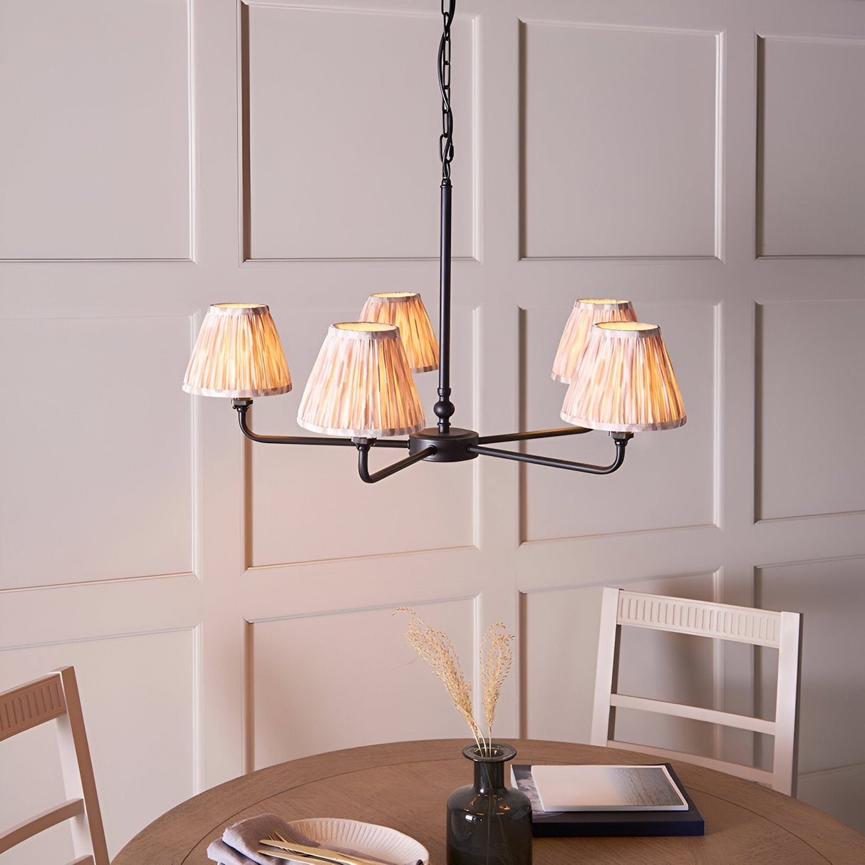 Caldmere 5 Light Ikat Pendant in Natural, matt black metal frame with five pleated fabric taper shades, shown above a dining table in a panelled room.