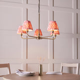 Endon Caldmere 5 light pendant with antique brass arms and coral pink pleated ikat tapered shades, hung above a dining table against panelled walls.