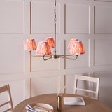 Endon Caldmere five light pendant with antique brass arms and coral pink pleated ikat tapered shades, hung above a wooden dining table.