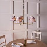 Caldmere 5 Light Ikat Pendant in antique brass with grey pleated fabric shades, hung above a dining table in a panelled room.