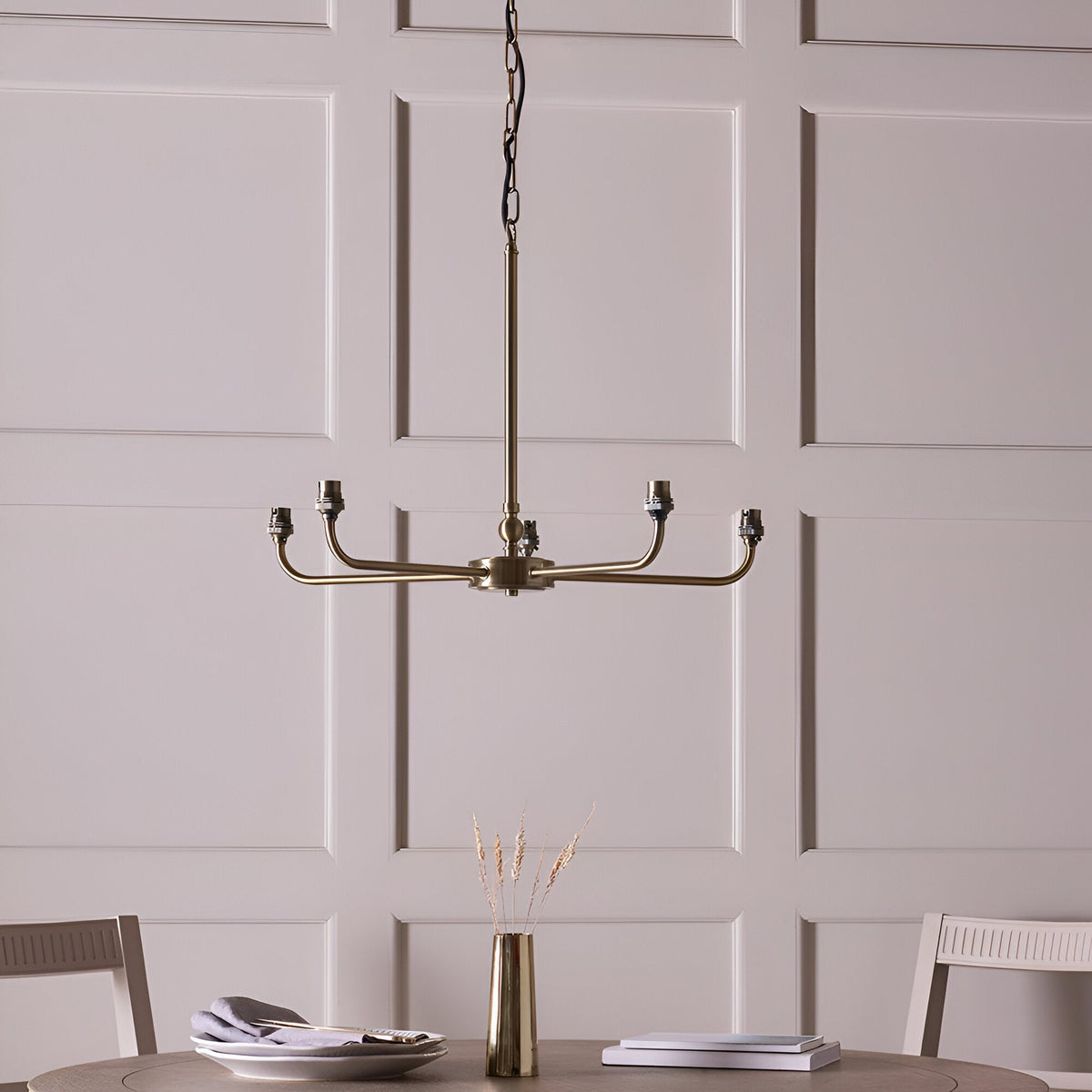Caldmere 5 Light Ikat Pendant in antique brass finish with five bare bulb holders on a spoke frame, shown hanging in a dining room above a table.