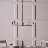 Caldmere 5 Light Ikat Pendant in antique brass finish with five bare bulb holders on a spoke frame, shown hanging in a dining room above a table.