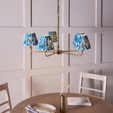 Endon Caldmere 5 light pendant with tapered pleated marlin blue ikat fabric shades on antique brass arms, shown above a dining table.