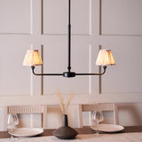 Endon Caldmere 2 light linear pendant in matt black with tapered natural pleated fabric shades, shown above a dining table against a panelled wall.