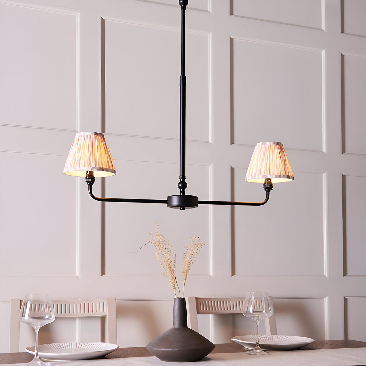 Endon Caldmere 2 Light Ikat Pendant in matt black with two tapered natural pleated shades on a linear frame, shown above a dining table.