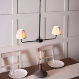 Endon Caldmere 2 light pendant with matt black linear frame and natural pleated tapered shades, shown above a dining table against panelled walls.