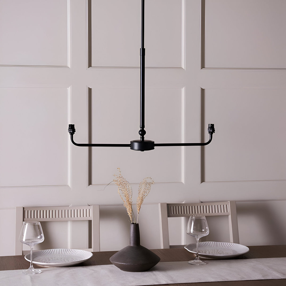 Endon Caldmere 2 light pendant frame in matt black, shown without shades on a telescopic stem above a panelled dining room wall.