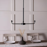 Endon Caldmere 2 light pendant frame in matt black, shown without shades on a telescopic stem above a panelled dining room wall.