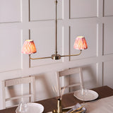 Endon Caldmere 2 light linear pendant in antique brass with coral pink pleated ikat tapered shades, shown above a wood dining table.