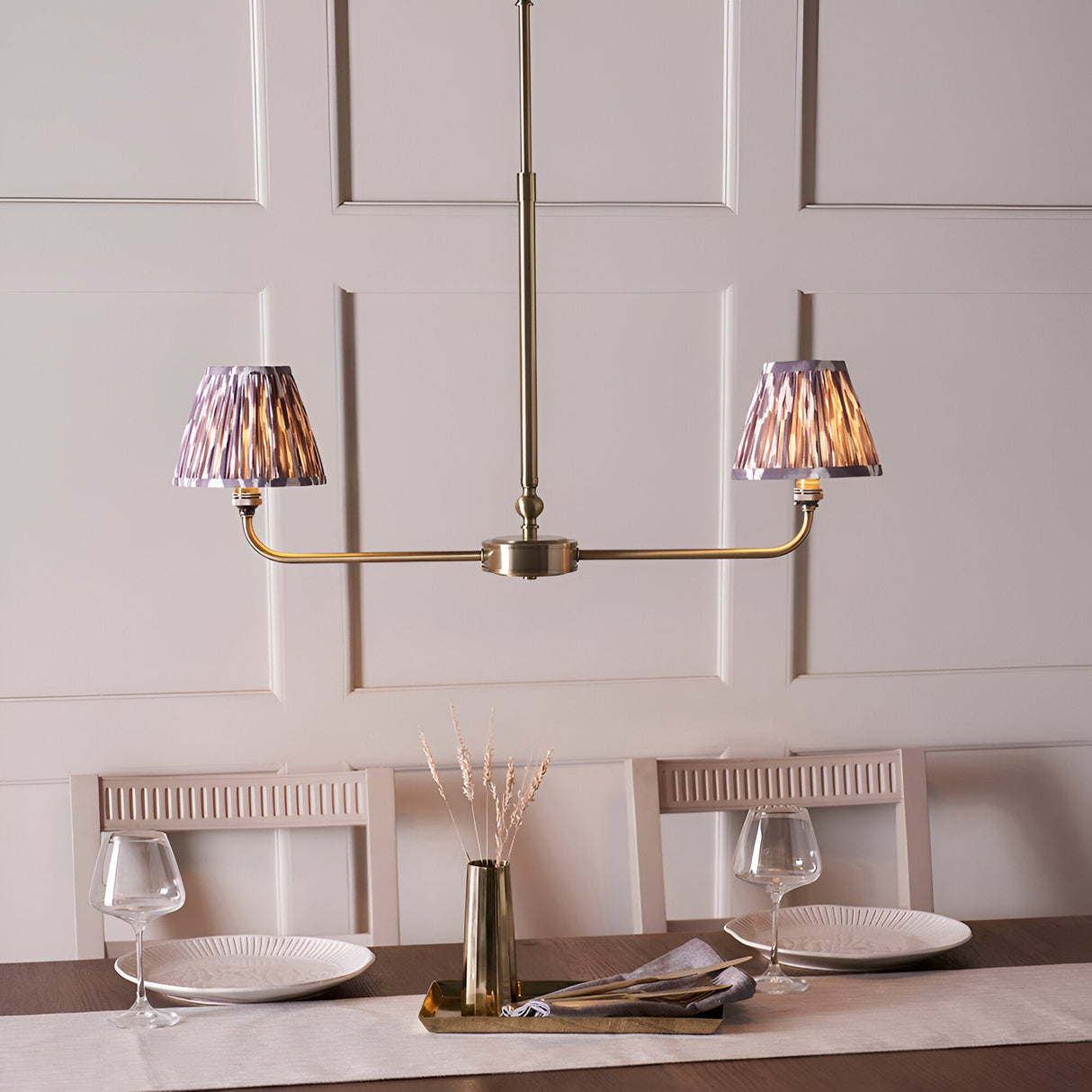 Caldmere 2 Light Ikat Pendant in Grey with antique brass linear frame and pleated tapered shades, shown above a dining table in a panelled room.