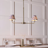 Caldmere 2 Light Ikat Pendant in antique brass with grey pleated tapered shades, shown above a dining table in a panelled room.