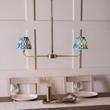 Endon Caldmere 2 light pendant in antique brass with twin tapered blue ikat pleated shades on a linear frame, shown above a dining table.