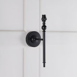 Endon Caldmere wall light base in matt black with slim upright stem, ball detail and B22 lamp holder, mounted on white panelled wall, shade not fitted.