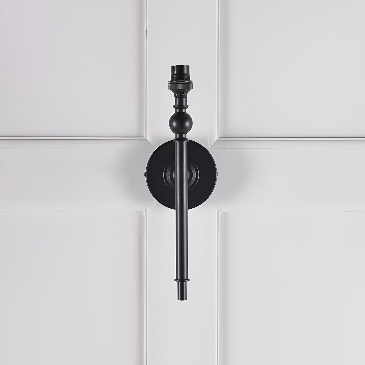 Endon Caldmere wall light base in matt black with slim tapered stem, ball detail and B22 lamp holder, shown without shade on white panelled wall.