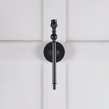 Endon Caldmere wall light base in matt black with slim tapered stem, ball detail and B22 lamp holder, shown without shade on white panelled wall.