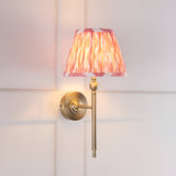 Caldmere Ikat Wall Light in Coral with a pleated tapered fabric shade on an antique brass wall-mounted arm, shown against a light panelled wall.