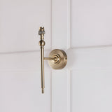 Caldmere Ikat Wall Light in antique brass, shown without its shade, mounted on a light panelled wall with a round backplate and slim upright arm.
