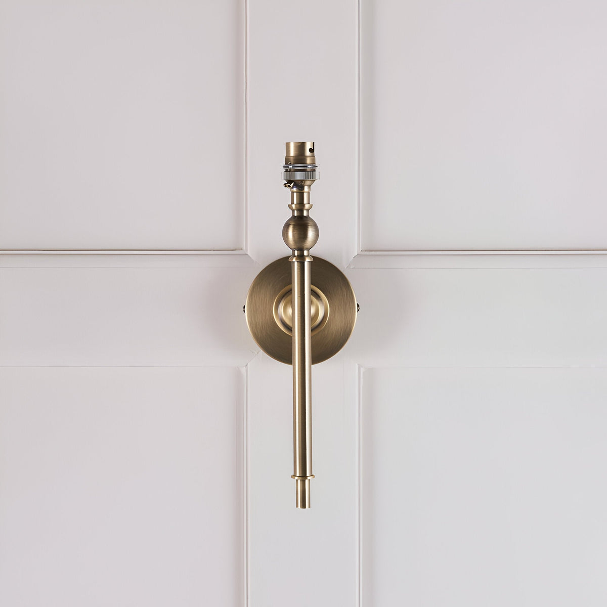 Caldmere Ikat wall light in antique brass with slim adjustable arm and B22 lamp holder, shown without shade against a light panelled wall.