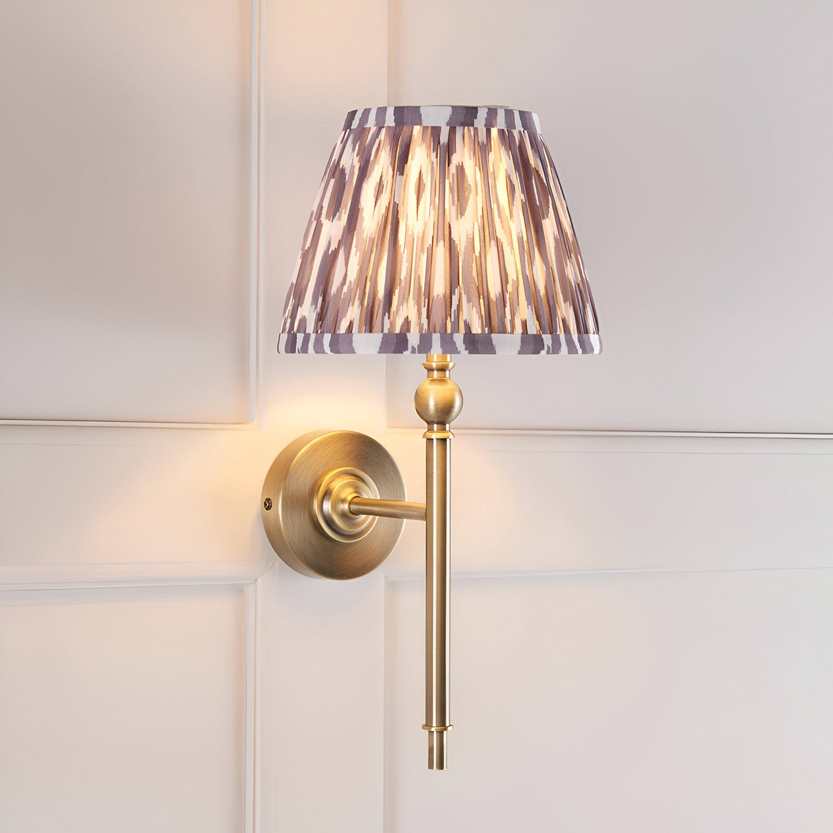 Endon Caldmere wall light with a pleated grey Ikat tapered shade and antique brass arm, mounted on a white panelled wall.