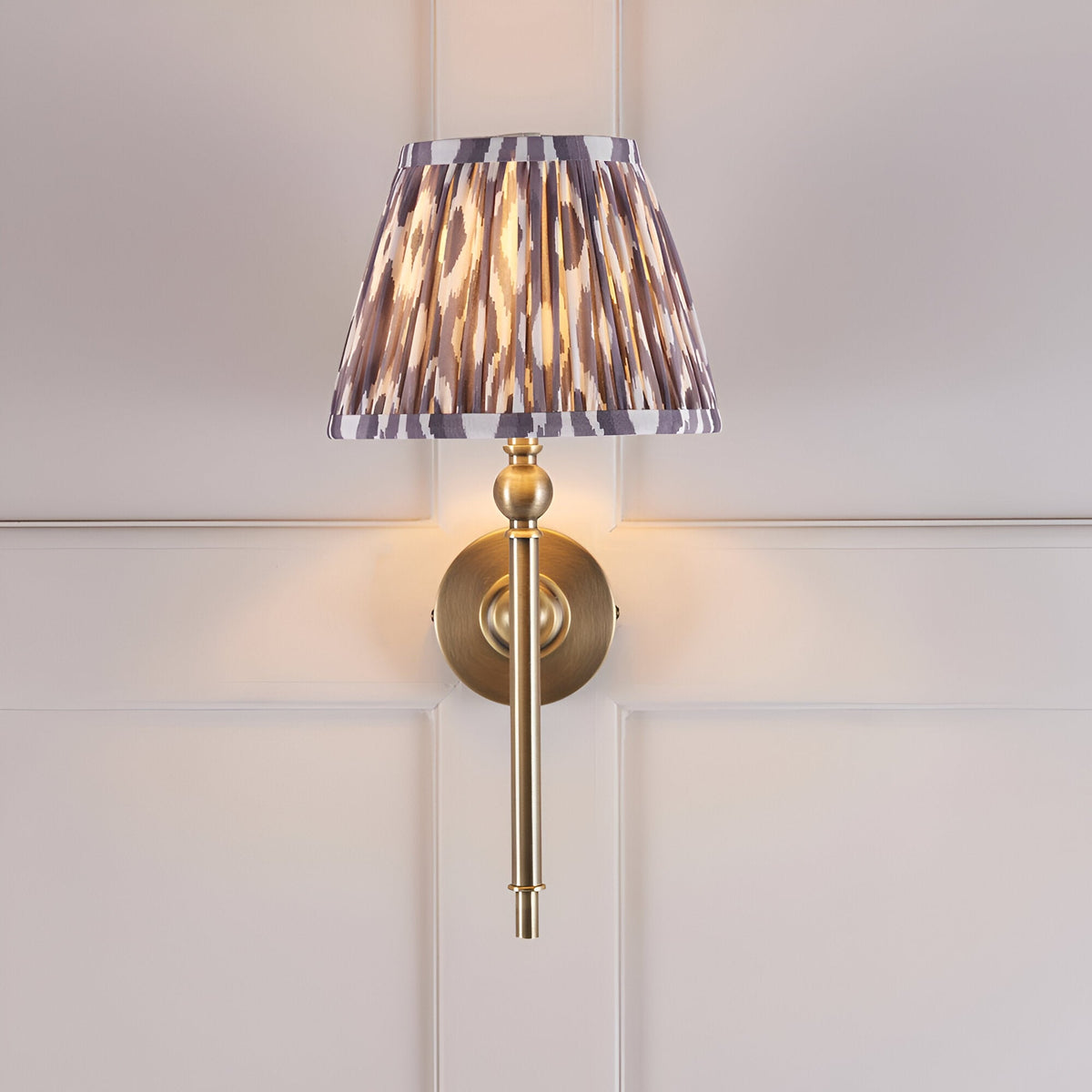 Endon Caldmere wall light with a pleated grey Ikat tapered shade and antique brass arm, mounted on a panelled wall.