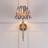 Endon Caldmere wall light with a pleated grey Ikat tapered shade and antique brass arm, mounted on a panelled wall.