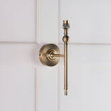 Endon Caldmere wall light base in antique brass with slim arm and B22 lamp holder, shown without shade against white panelled wall.