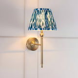 Caldmere Ikat Wall Light in antique brass with a pleated blue patterned fabric tapered shade, mounted on a wall-panelled background.