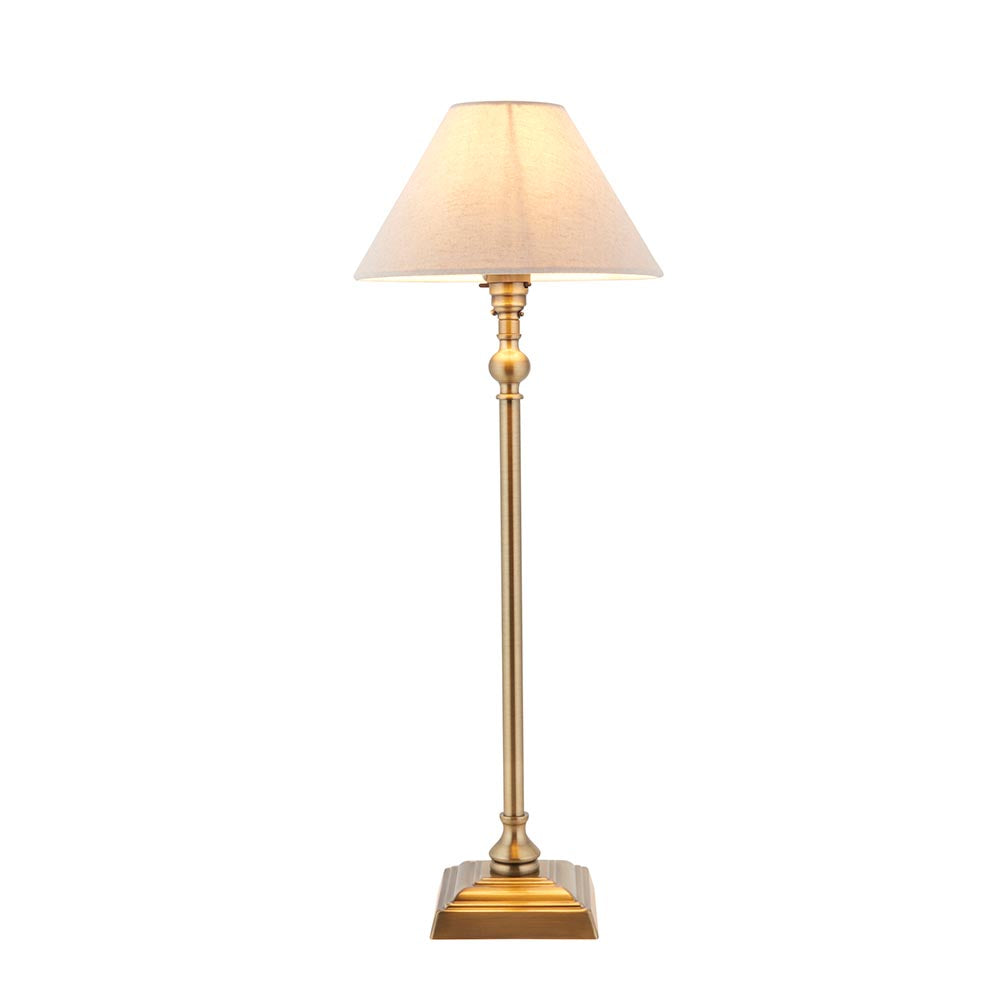 Endon Caldmont candlestick table lamp in antique brass with a tapered natural linen shade, slim upright column and stepped square base, on a white background.