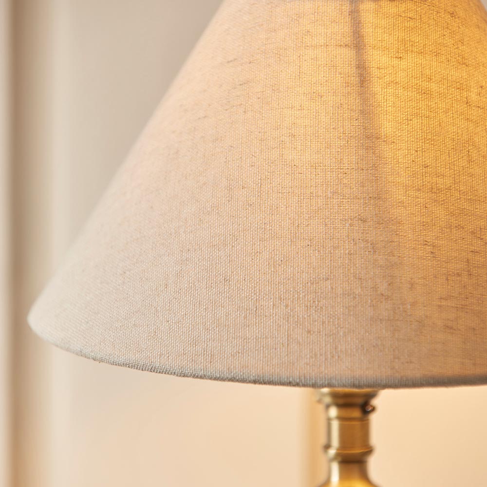 Close-up of the Endon Caldmont table lamp showing its tapered natural linen mix shade and antique brass candlestick-style holder.