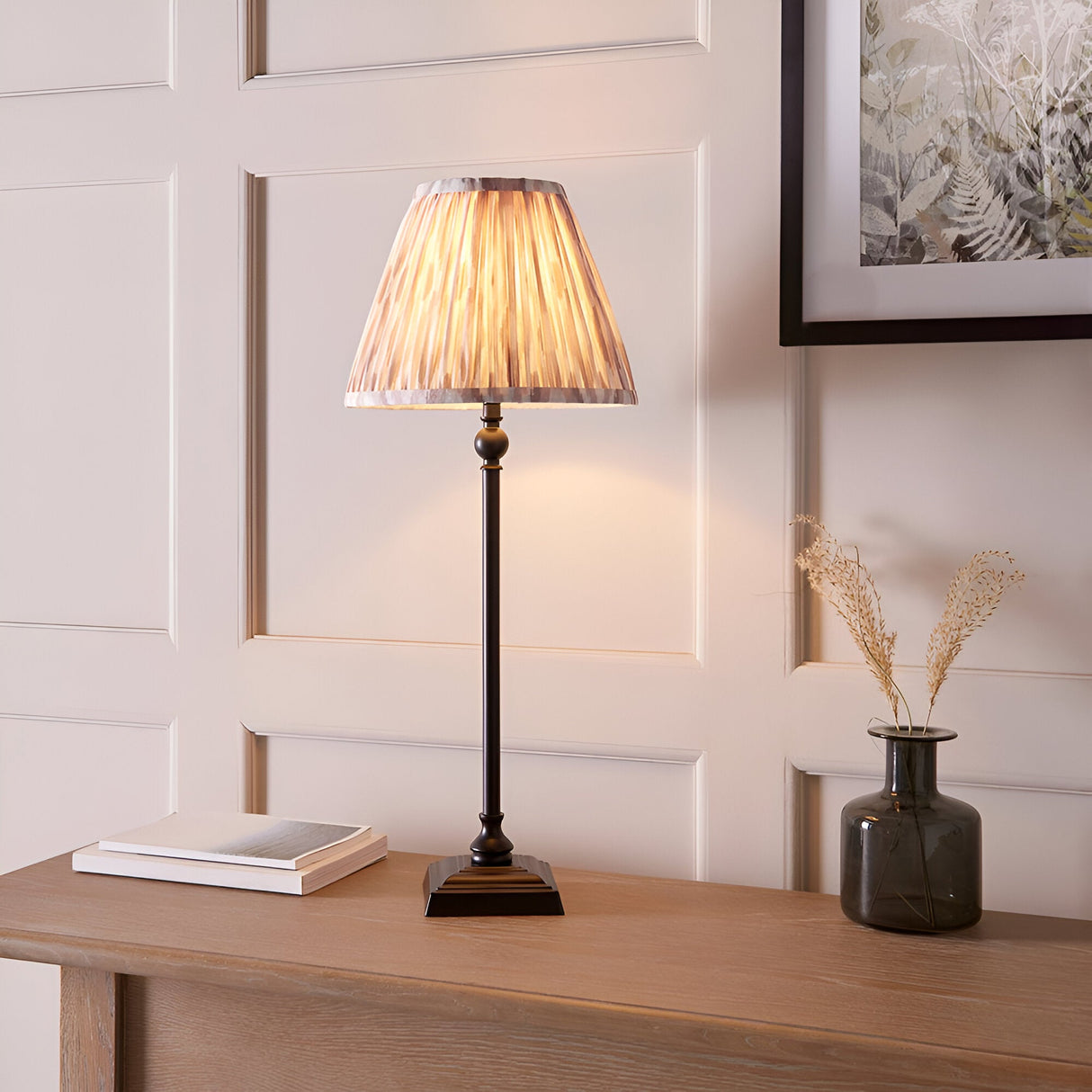 Caldmere Ikat Table Lamp in Cream with pleated fabric shade on a matt black candlestick-style base, shown lit on a wooden console table.