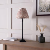 Caldmere Ikat Table Lamp with slim matt black candlestick base and pleated cream-toned patterned shade, shown on a wooden console beside a vase and books.