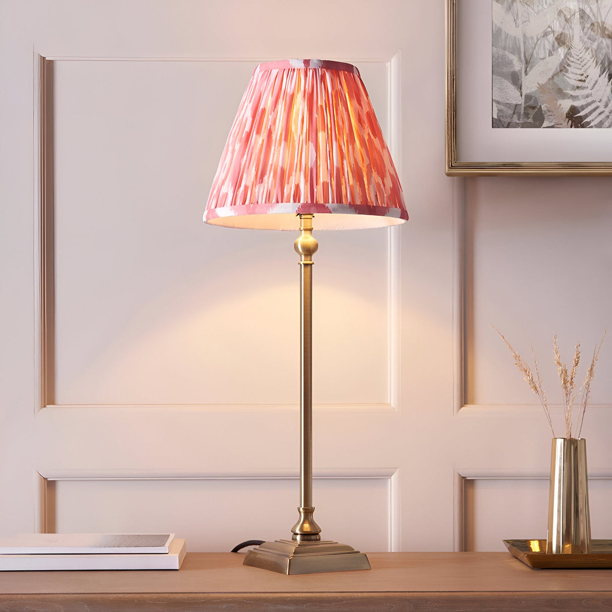 Caldmere Ikat Table Lamp in Coral with pleated fabric shade on an antique brass candlestick-style base, shown lit on a console table.