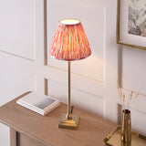 Caldmere Ikat Table Lamp in coral with a pleated fabric shade on an antique brass candlestick-style base, shown on a wooden console table.