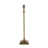 Caldmere table lamp base with slim turned candlestick-style stem, square foot in antique brass plate, and B22 holder, shown without shade on a white background.