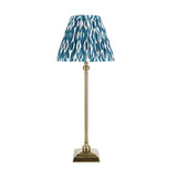 Endon Caldmere table lamp with slim antique brass candlestick base and pleated blue Ikat print shade on a plain white background.