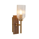 Bramton wall light with a grooved walnut-stained wood backplate, brass arm and clear ribbed glass shade, shown lit against a plain white background.