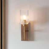 Bramton Wall Light in brass with a ribbed clear glass shade and grooved walnut-stained wood backplate, mounted lit on a plain wall.