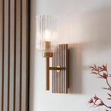 Bramton Wall Light in brass with a ribbed glass shade, brass arm and grooved wood backplate, mounted on a light wall beside a wooden slatted panel.