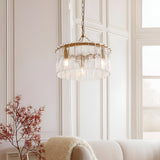 Brockhurst 3 Light Pendant in brass with drum-shaped textured glass panels, hung from a chain in a light-toned living room with a cream sofa nearby.