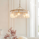 Endon Brockhurst 5 light pendant in brushed aged brass with textured glass panels in a drum ring, hanging from a chain in a bright panelled room.